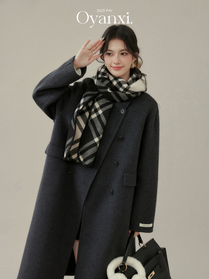 Model wearing a dark charcoal coat with a black-and-white plaid scarf and handbag