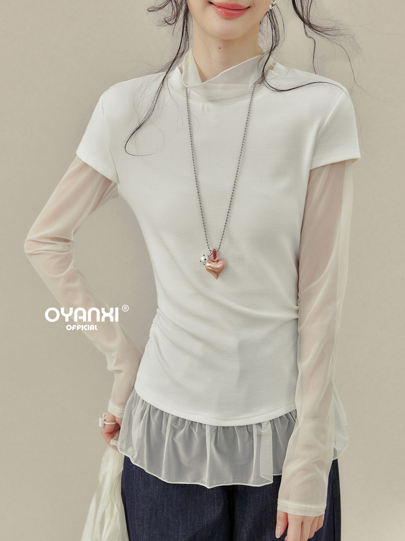 Model wearing a white layered long-sleeve top with sheer sleeves and a heart pendant necklace