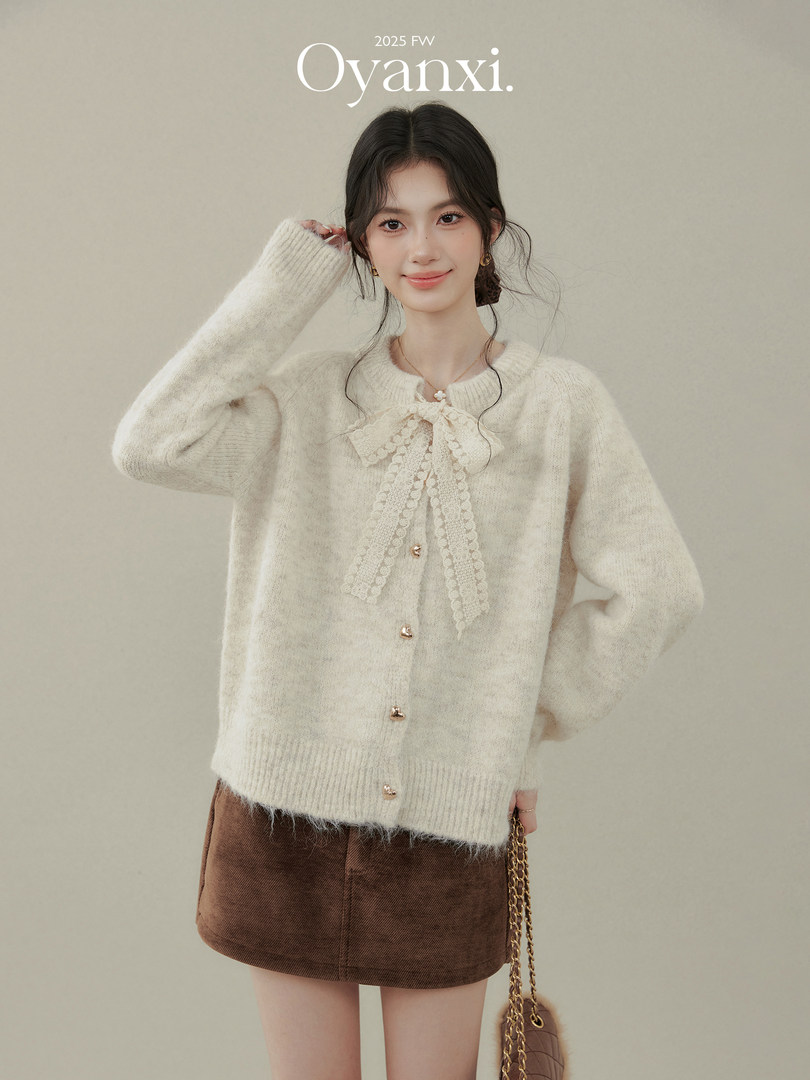 Model wearing a cream fuzzy cardigan with lace bow detail and a brown mini skirt