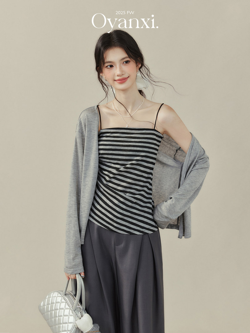 Model wearing a black-and-gray striped camisole with a gray cardigan and dark skirt, holding a silver quilted handbag