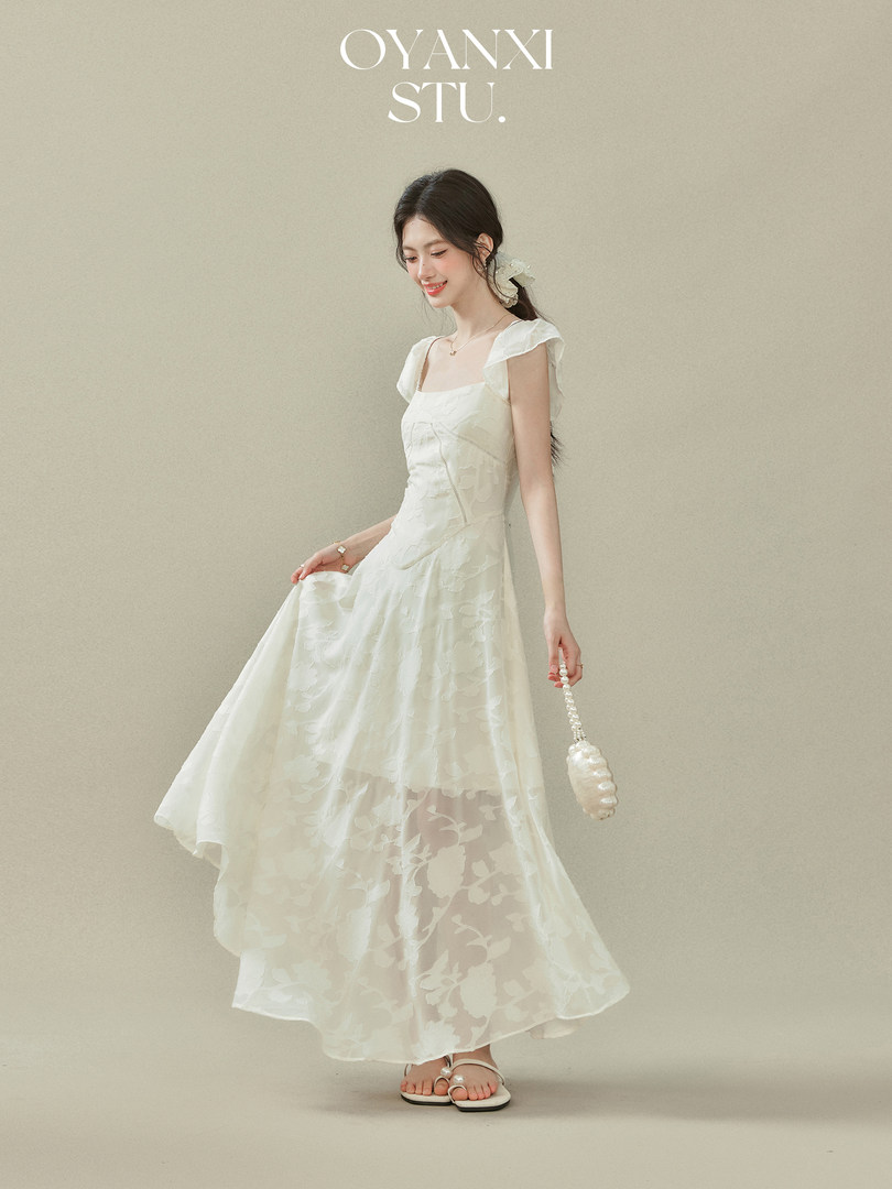 Woman wearing a white sleeveless flowy dress with sheer floral overlay