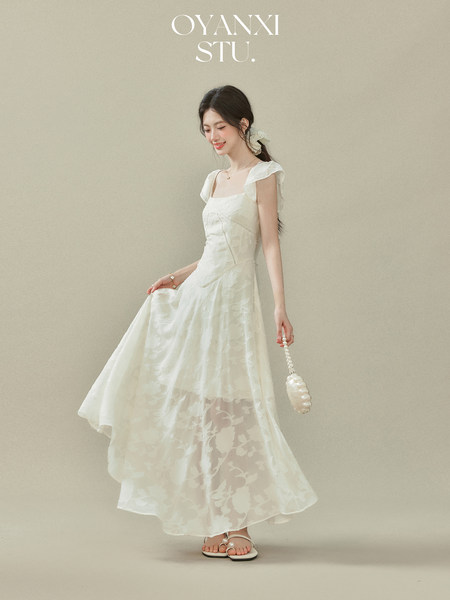 Woman wearing a white sleeveless flowy dress with sheer floral overlay