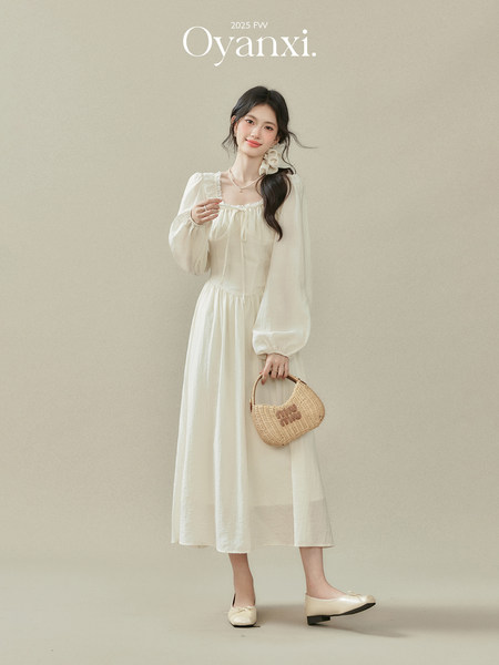 Woman wearing a white long-sleeve midi dress with a woven handbag and flats