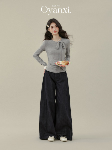 Model wearing a gray long-sleeve top with a bow detail, wide-leg dark pants, and white flats