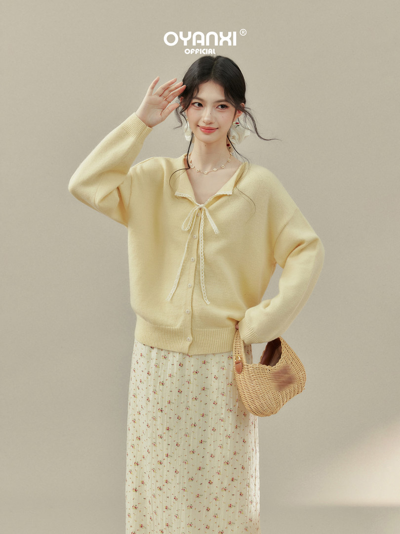 Woman wearing a pale yellow cardigan with a floral skirt and woven handbag