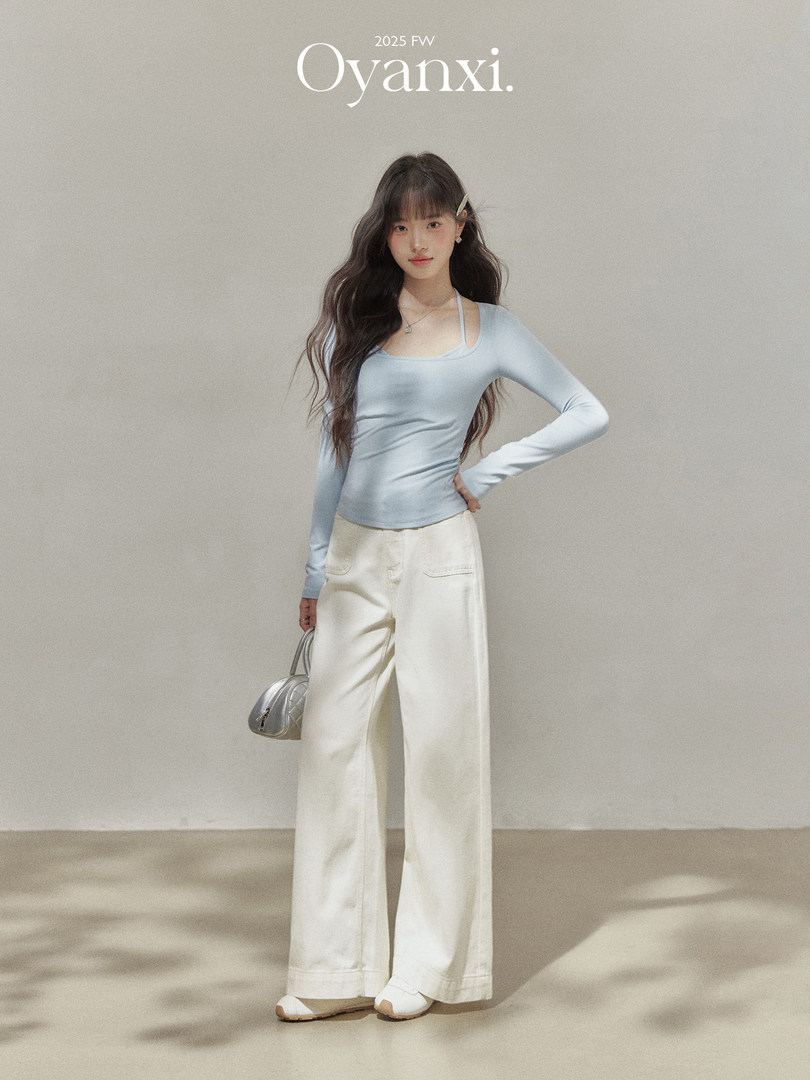 Model wearing a light blue long-sleeve top and cream wide-leg pants with a silver handbag