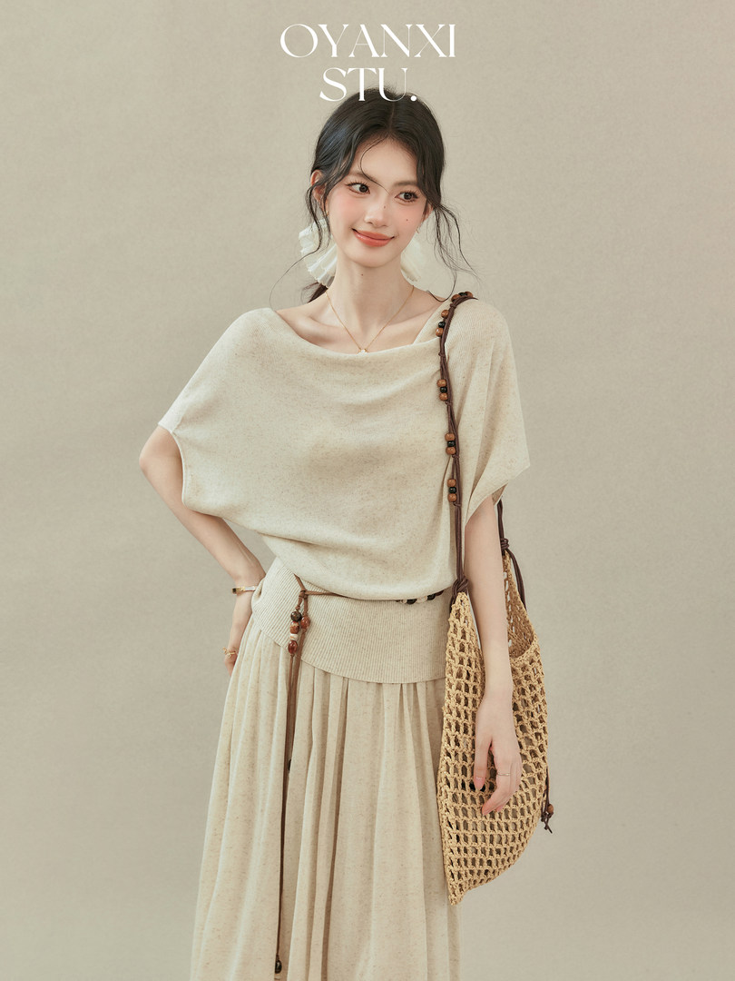 Woman modeling a beige knit top and matching skirt with a woven shoulder bag