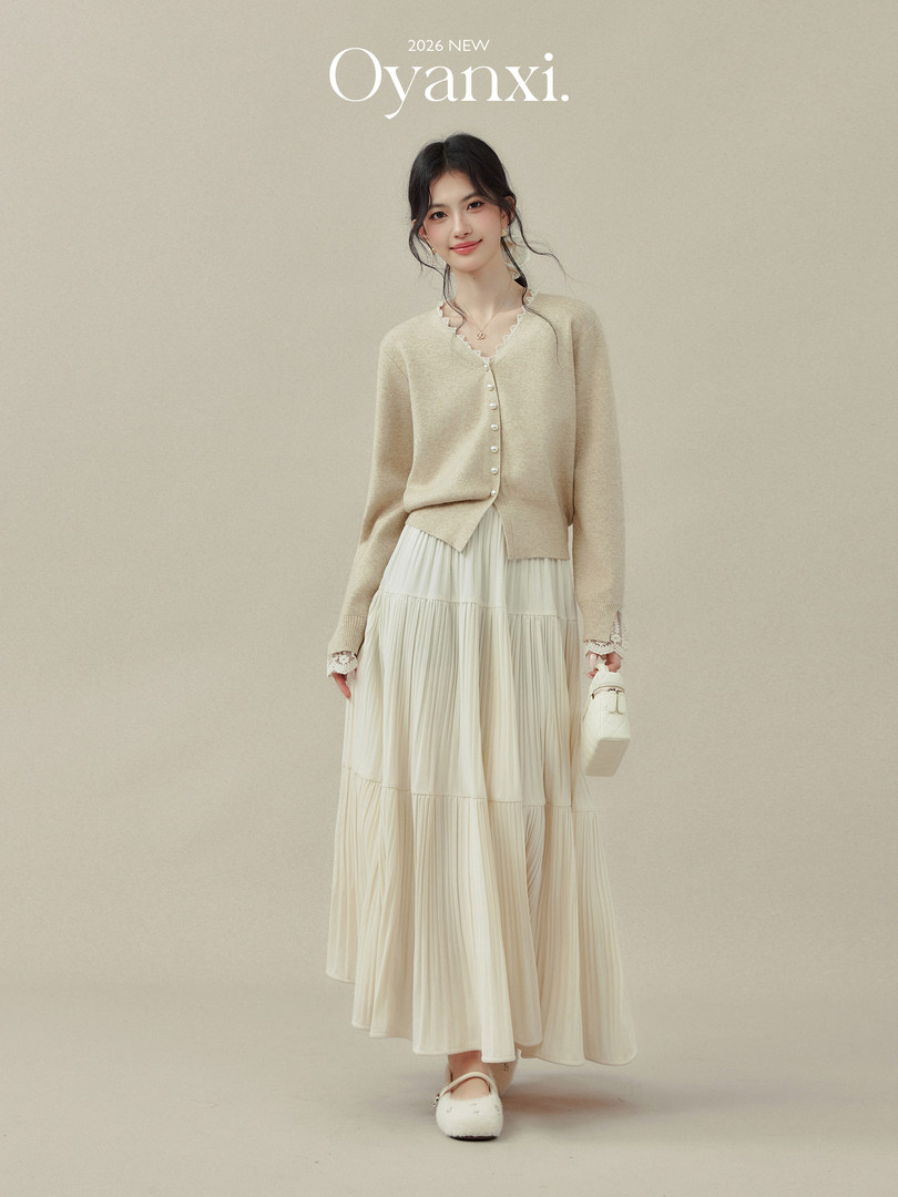 Model wearing a beige cardigan and cream pleated skirt with a small white handbag