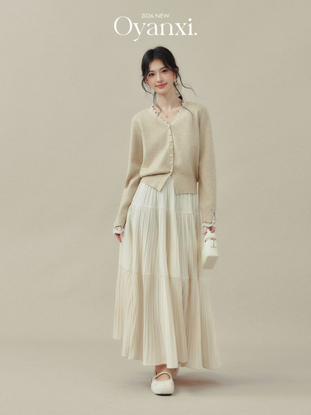 Model wearing a beige cardigan and cream pleated skirt with a small white handbag