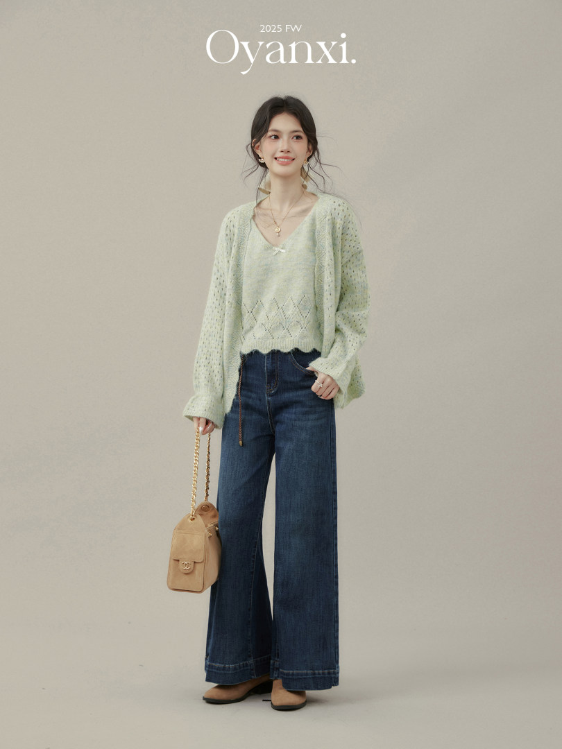 Model wearing a light green knit top and cardigan with wide-leg dark jeans and a beige shoulder bag