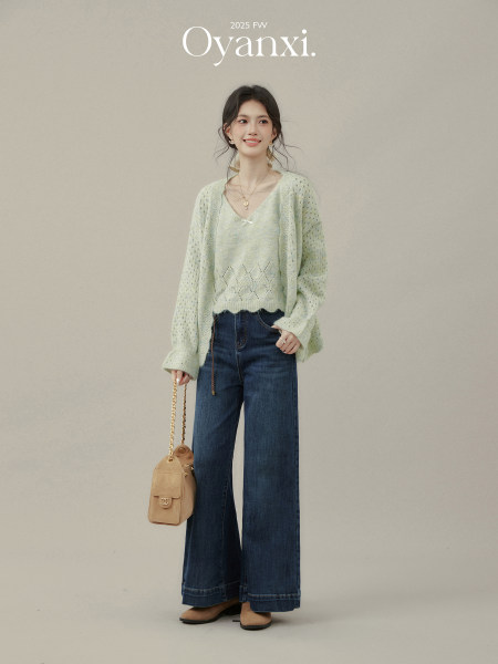 Model wearing a light green knit top and cardigan with wide-leg dark jeans and a beige shoulder bag