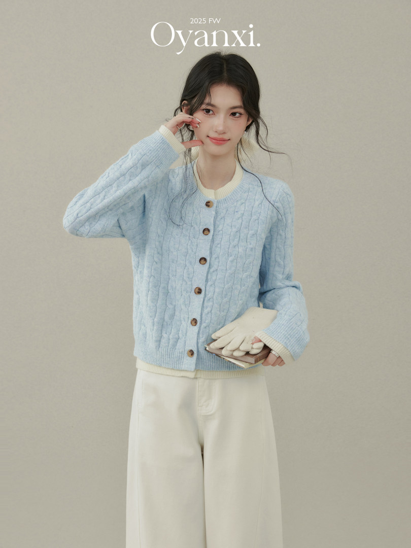 Model wearing a light blue cable-knit cardigan with cream trim and white pants
