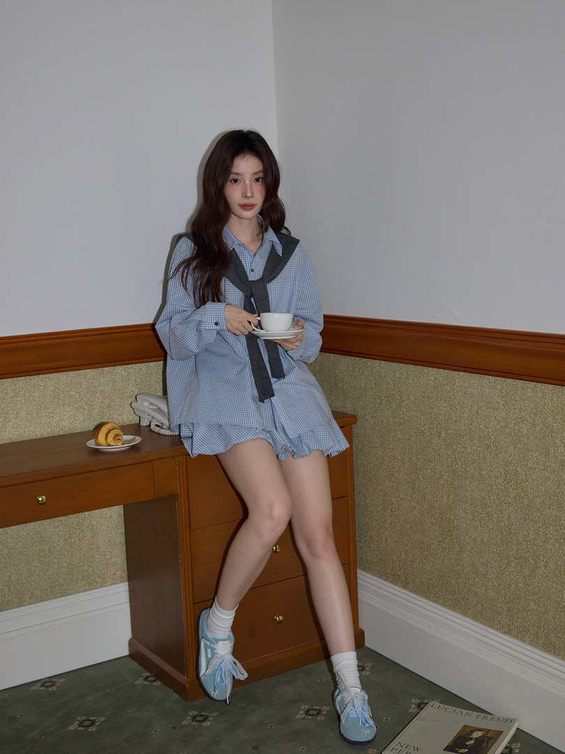 Model wearing a blue gingham shirt dress with a sweater tied at the waist and light blue sneakers