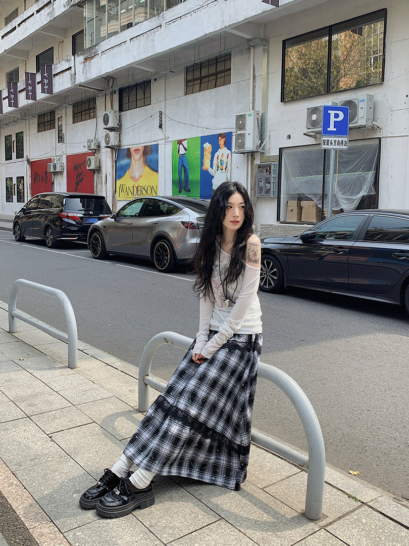 Model wearing a white long-sleeve top with a black plaid maxi skirt and black shoes on a street