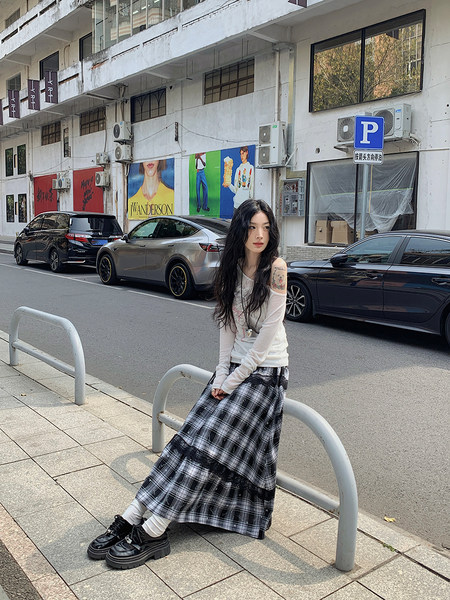 Model wearing a white long-sleeve top with a black plaid maxi skirt and black shoes on a street