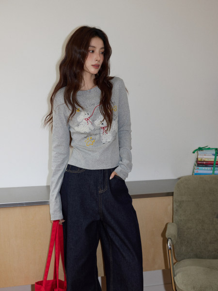 Model wearing a gray graphic long-sleeve top with dark wide-leg jeans