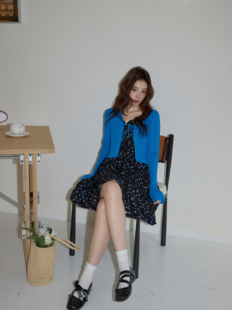 Model wearing a bright blue cardigan over a black floral dress with black loafers
