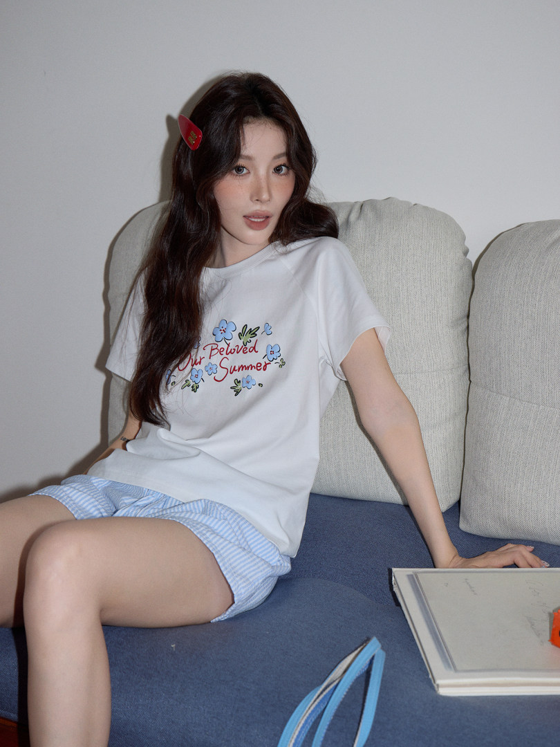 Woman wearing a white graphic T-shirt and striped shorts while sitting on a sofa