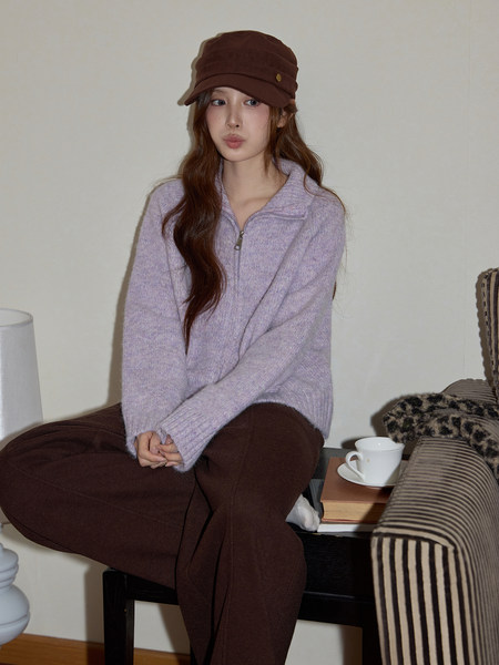 Woman wearing a lavender knit zip-up sweater with brown pants and a brown cap