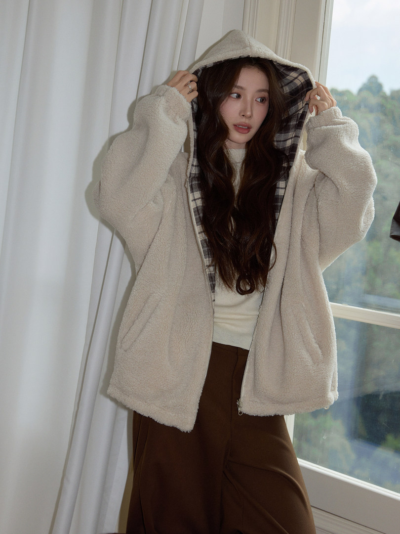 Model wearing a cream sherpa hooded jacket with plaid lining and brown pants