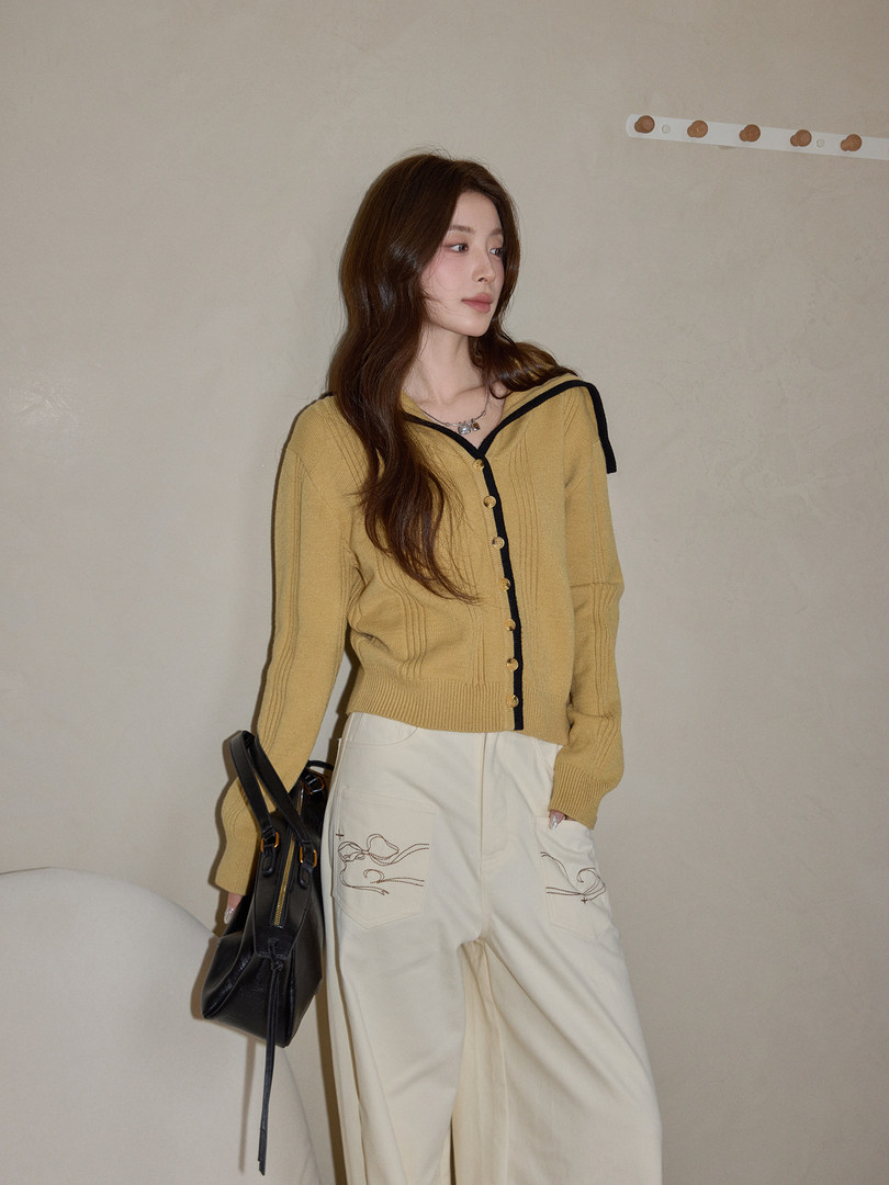 Model wearing a mustard sailor-collar knit top with cream pants and a black handbag