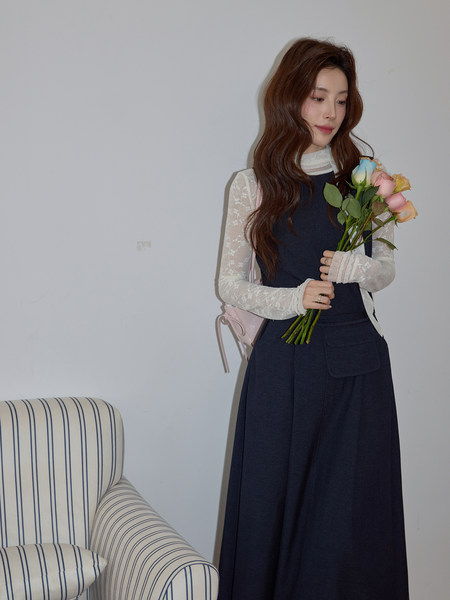 Woman wearing a navy sleeveless dress with a white lace long-sleeve top, holding flowers