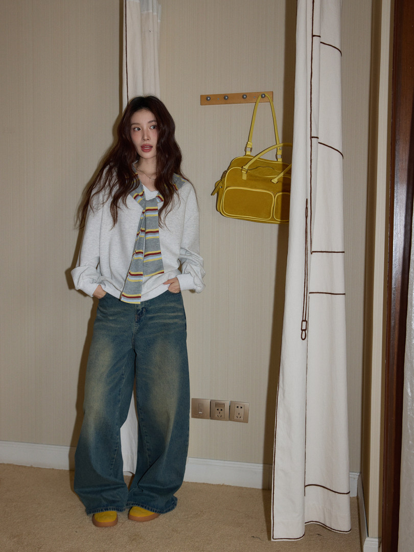 Model wearing a light sweater with striped scarf detail, wide-leg jeans, and a yellow handbag