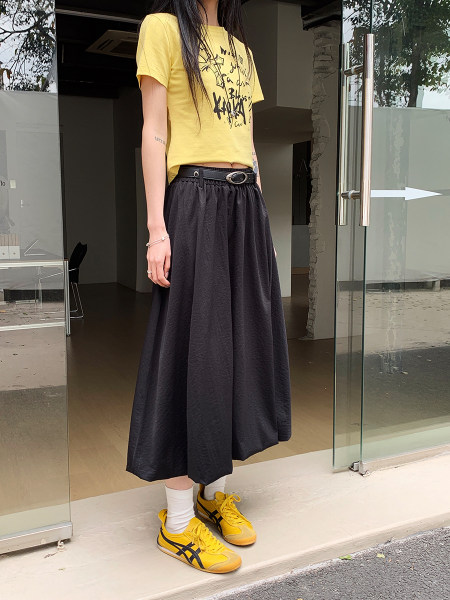 Model wearing a yellow graphic T-shirt with a long black skirt and yellow sneakers