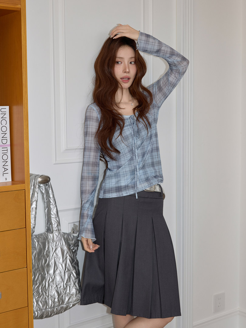 Woman modeling a blue plaid sheer long-sleeve top with a dark pleated skirt