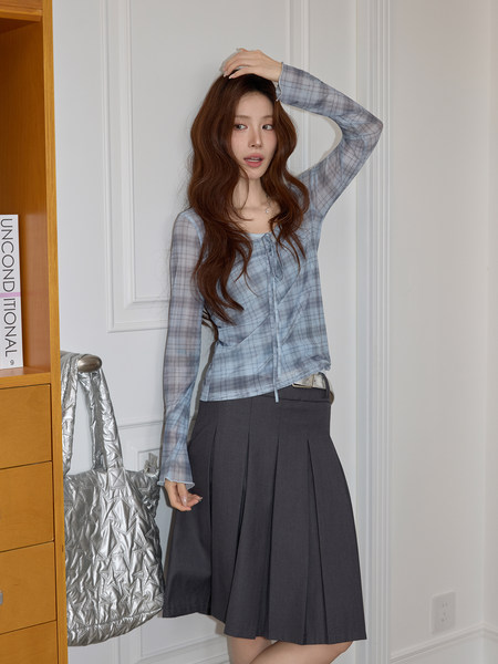 Woman modeling a blue plaid sheer long-sleeve top with a dark pleated skirt
