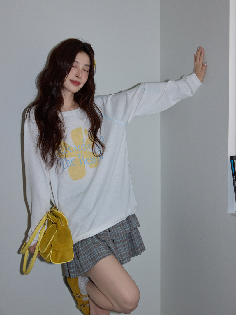 Model wearing a white graphic long-sleeve top with plaid skirt and yellow handbag