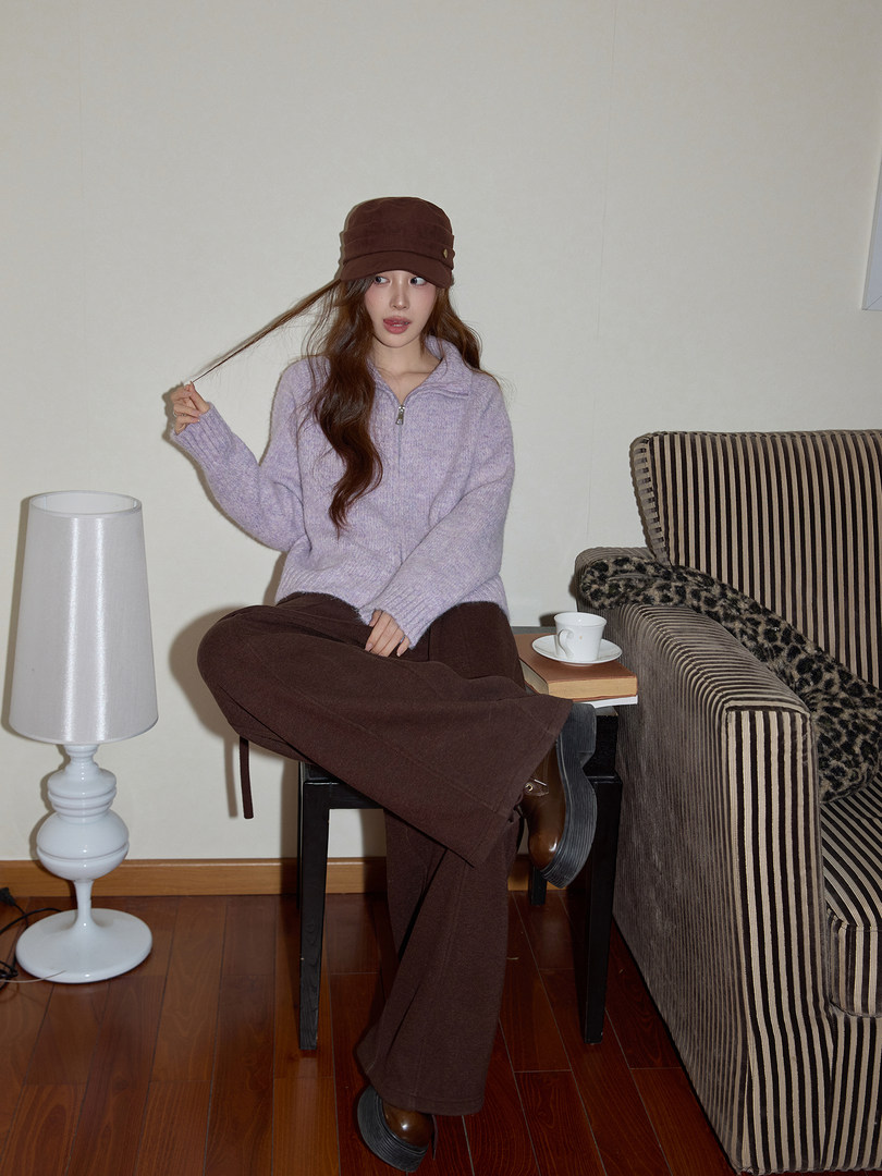 Woman modeling a lavender knit sweater, brown wide-leg pants, and a brown cap indoors
