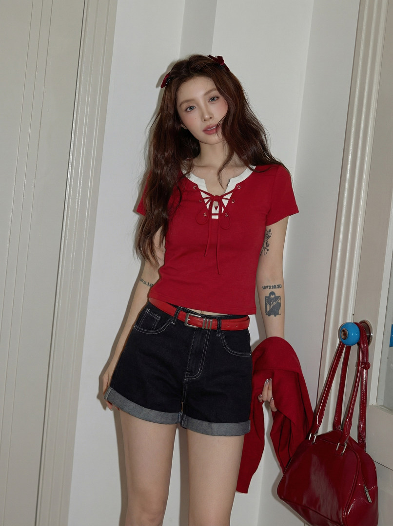Model wearing a red lace-up short-sleeve top with black denim shorts