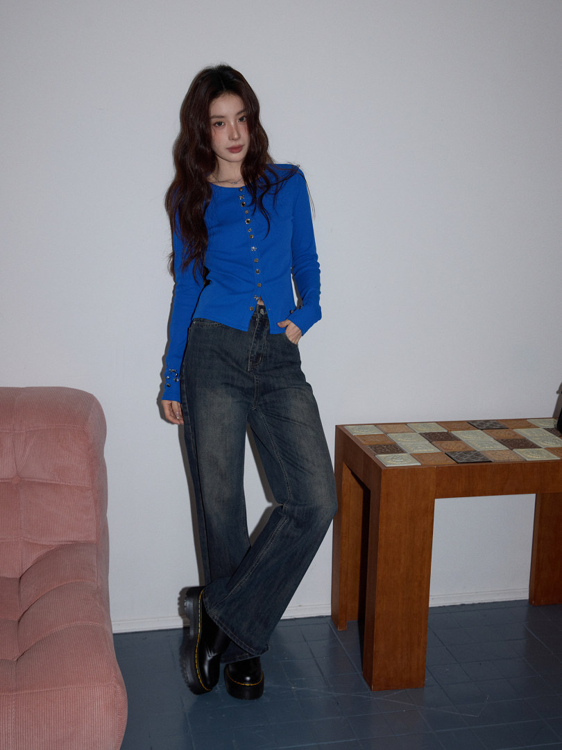 Woman wearing a blue long-sleeve button-front top with dark jeans and black boots.