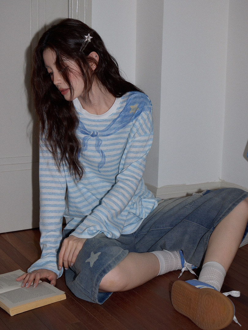 Model wearing a light blue striped long-sleeve top with a denim skirt
