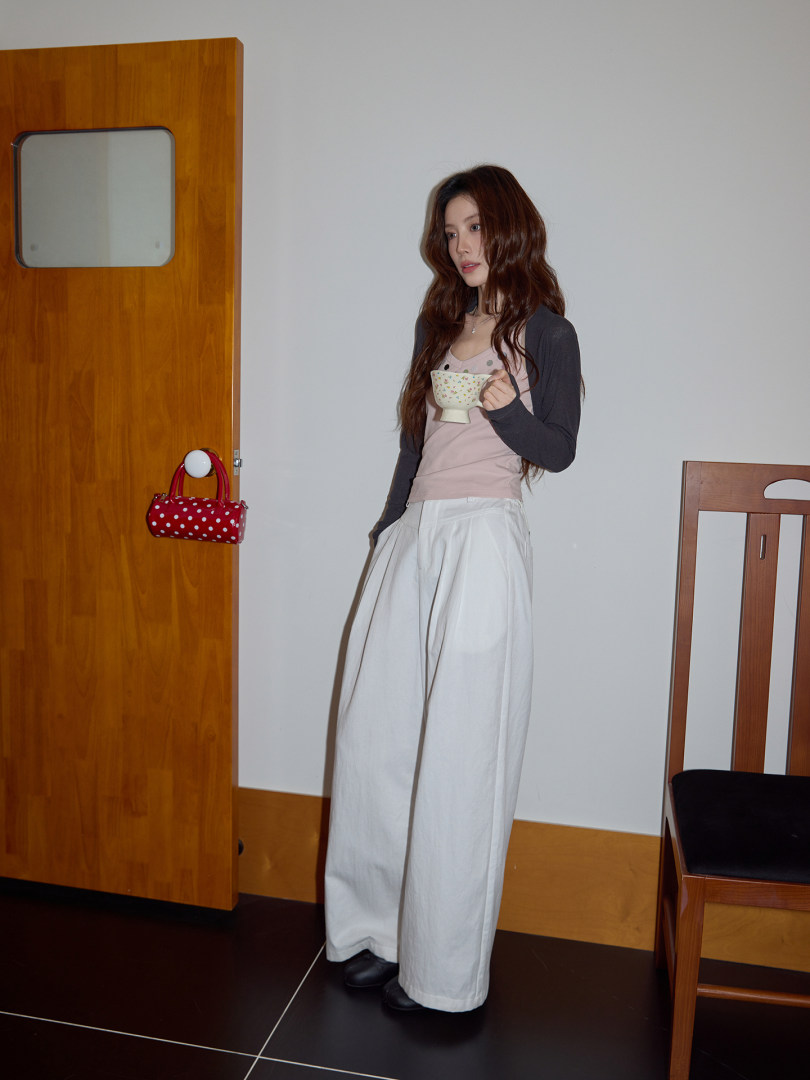 Model wearing a layered casual outfit with wide-leg white pants and a small handbag