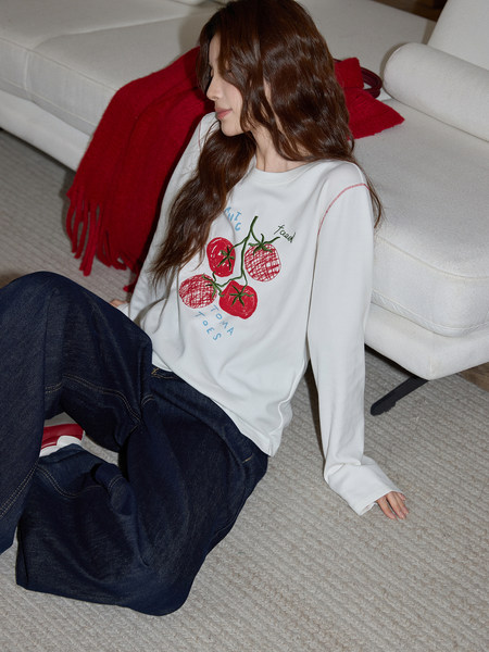 Woman wearing a white long-sleeve graphic top with tomato print and dark jeans