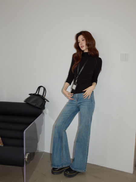 Woman wearing a black fitted top with flared blue jeans and black shoes