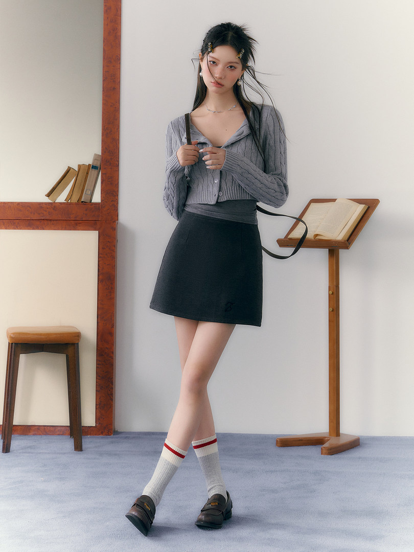 Model wearing a gray knit cardigan with a black mini skirt and loafers