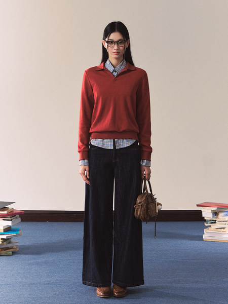 Model wearing a red sweater over a plaid shirt with wide-leg dark pants and a small brown handbag