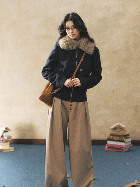 Model wearing a dark winter jacket with fur collar, wide-leg pants, and a crossbody bag