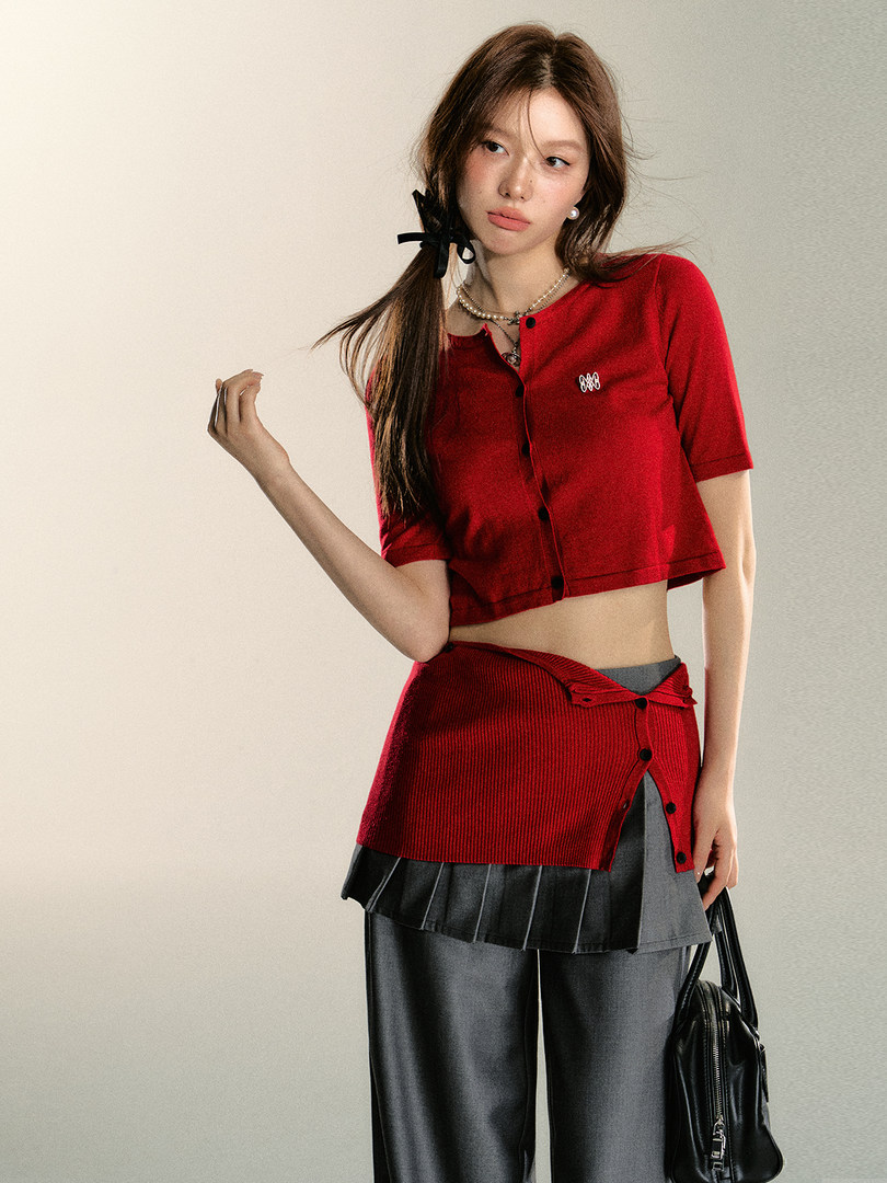 Model wearing a red cropped cardigan with layered skirt and gray pants