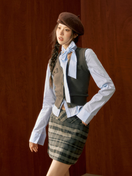 Model wearing a layered fall outfit with beret, shirt, vest, and plaid skirt