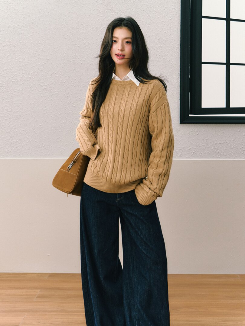Model wearing a tan cable-knit sweater with dark wide-leg jeans and a brown bag