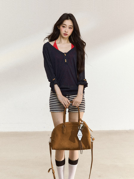 Model wearing a navy top and striped shorts while holding a brown handbag