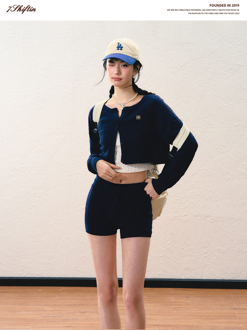 Model wearing a navy cropped cardigan with black shorts and a beige LA cap