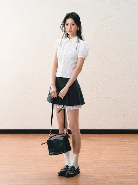 Model wearing a white puff-sleeve blouse with a black pleated skirt and black loafers.