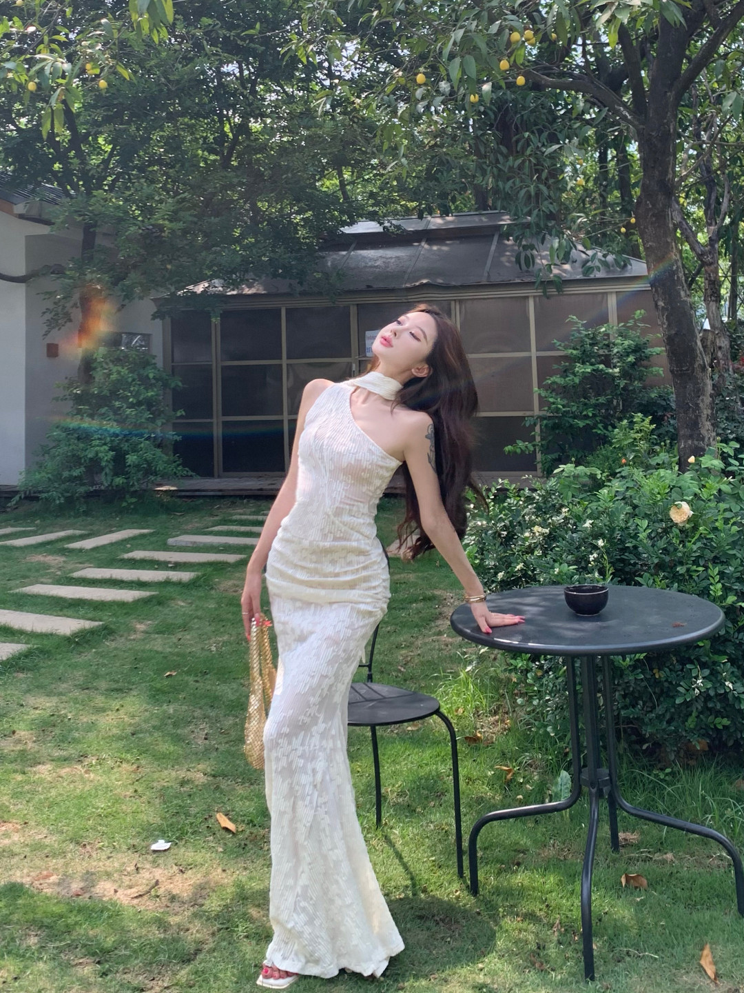 ชุดเดรสสายเดี่ยวไหล่เฉียง ผ้าไหมพิมพ์ลายดอกไม้สีขาวนวล กระโปรงหางปลาเก็บเอว ใส่แล้วดูผอมเพรียว ยาวเลยเข่า โชว์สะโพกอย่างสวยสง่า