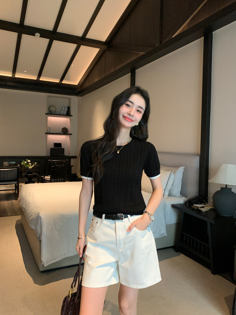 Woman wearing a black short-sleeve top and white shorts in a bedroom setting