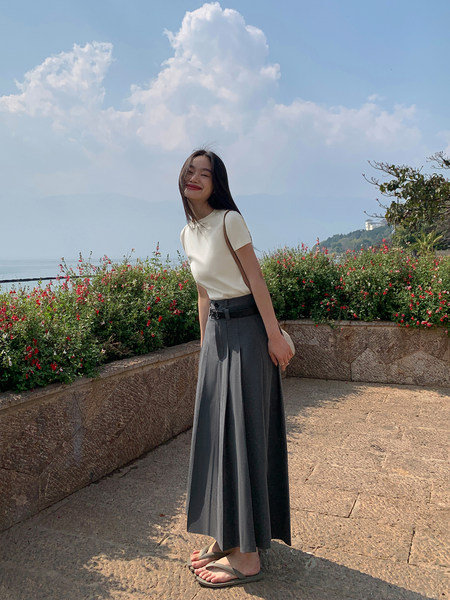 Woman modeling a white short-sleeve top with a gray pleated maxi skirt outdoors